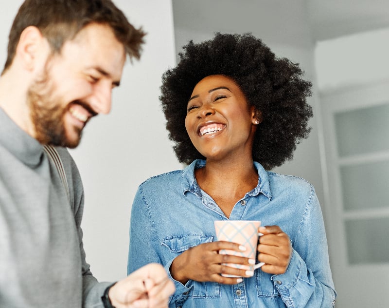 Couple talking, woman is holding a cup of coffee. They look happy. This couple uses mirror neurons to help improve conflict resolution in their marriage.