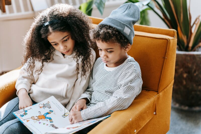 girl and boy reading a book together in chair